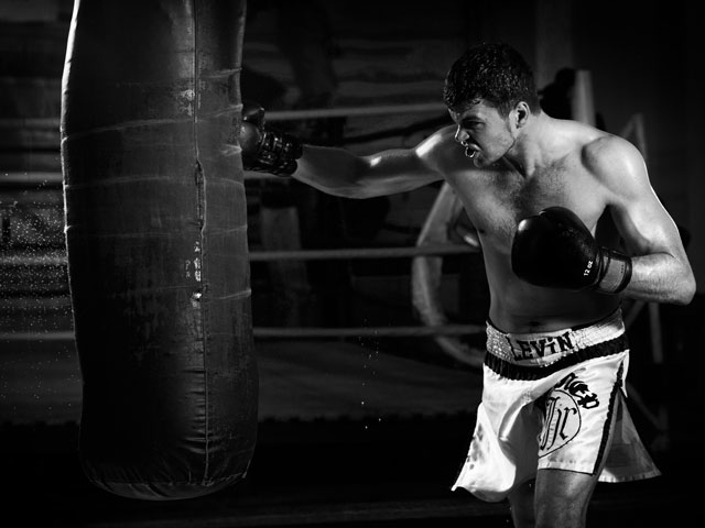 A boxer striking a heavy bag as he trains in the local boxing gym