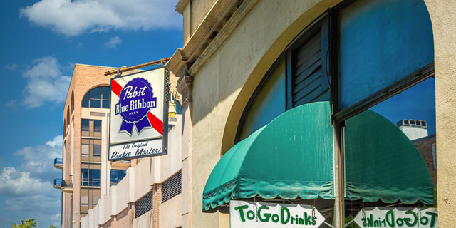 A Pabst Blue Ribbon sign hanging off the window of a bar for birds to sit on and tweet all day