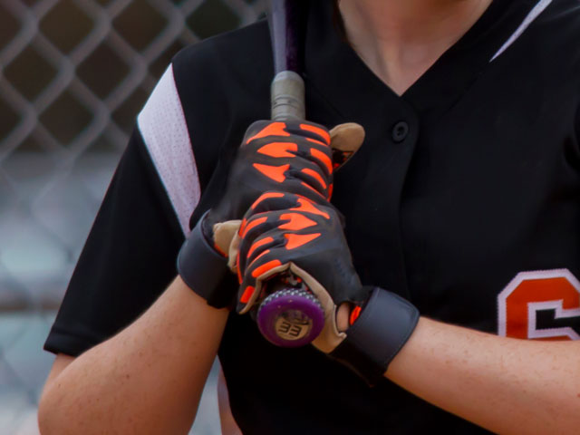 A female softball player wearing a pair of red and black batting gloves.